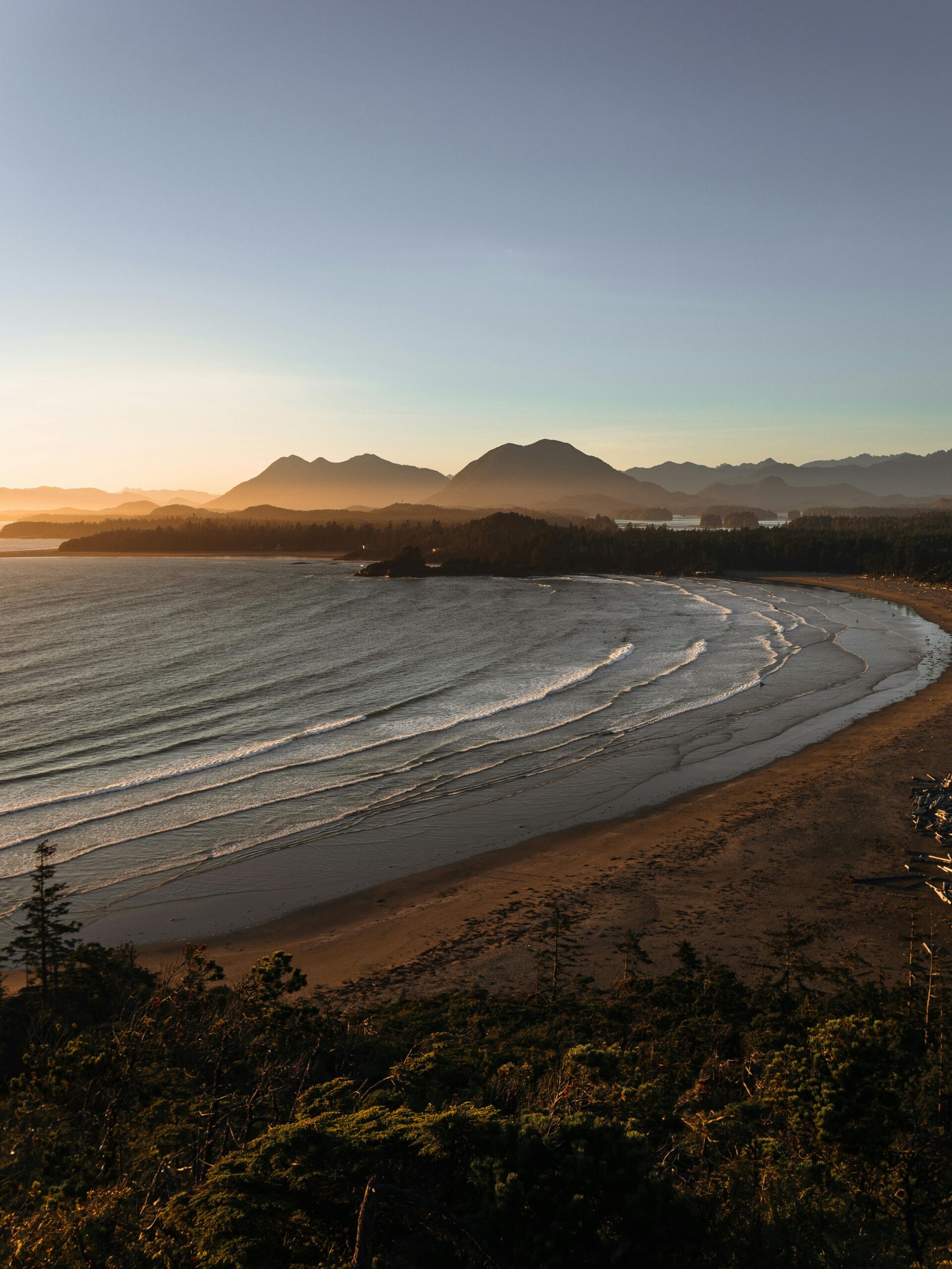 A tranquil aerial view of Tofino's beach and coastline during sunset, showcasing natural beauty and serene waters.