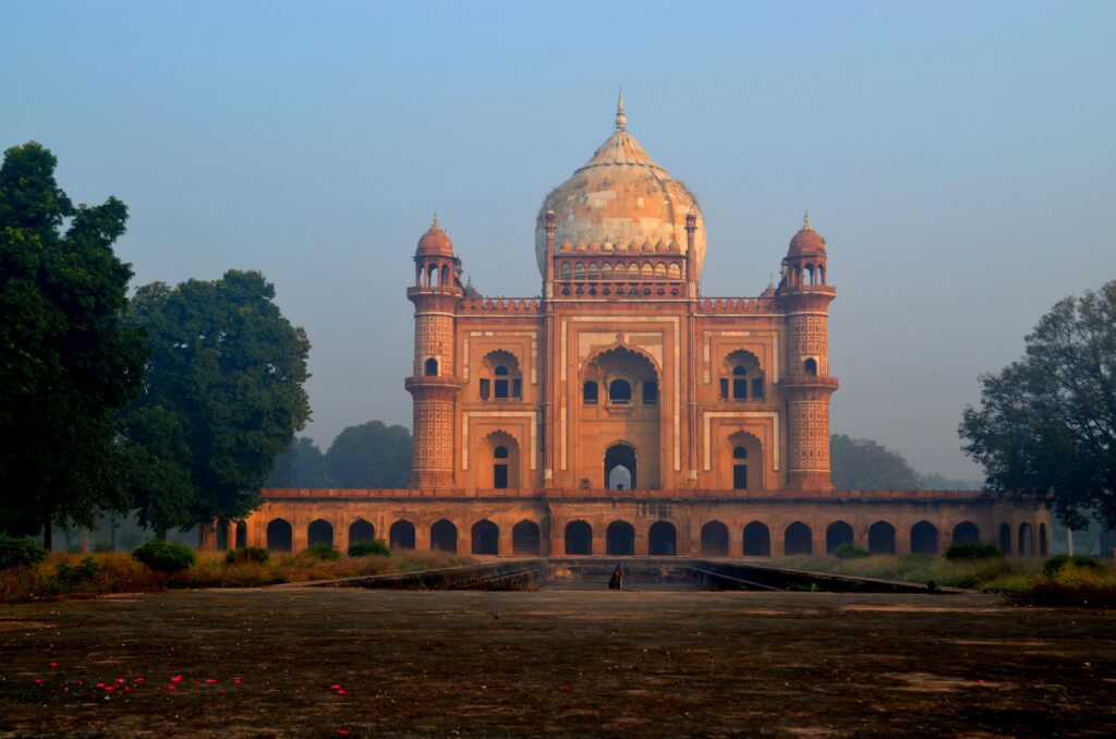 View of Safdarjung Tomb, a historical monument in New Delhi, surrounded by lush trees during sunrise.