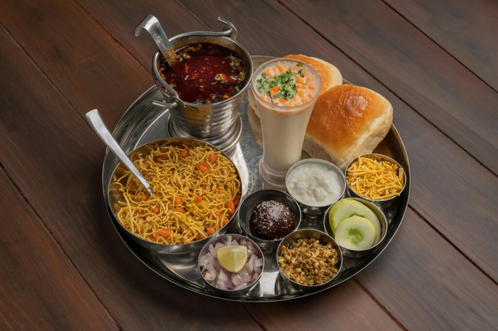 High-angle view of a traditional Indian thali featuring misal pav with various accompaniments.